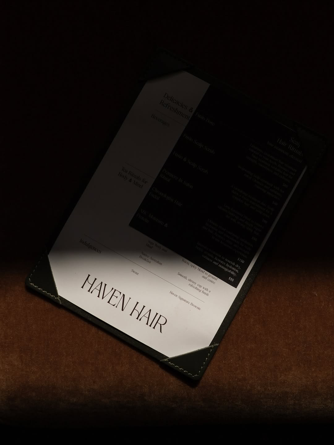 Menu or flyer on a table at Haven Hair salon, partially obscured, with a dark background illuminating the lower part of the paper.