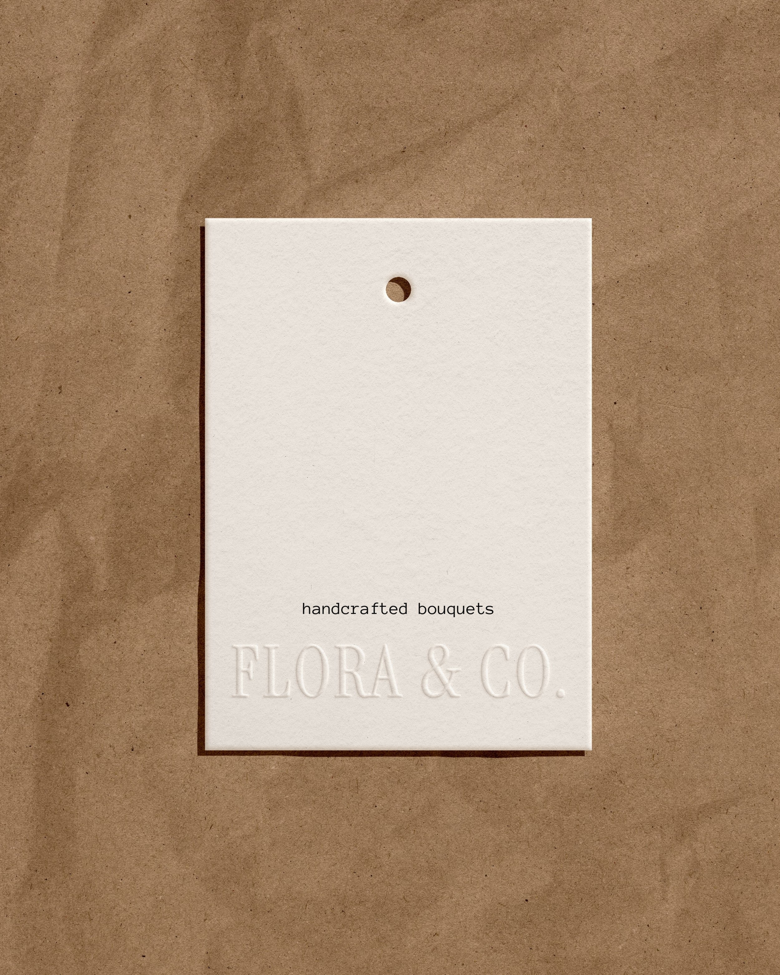 White tag with 'handcrafted bouquets' and 'FLORA & CO.' embossed text, on brown paper background.