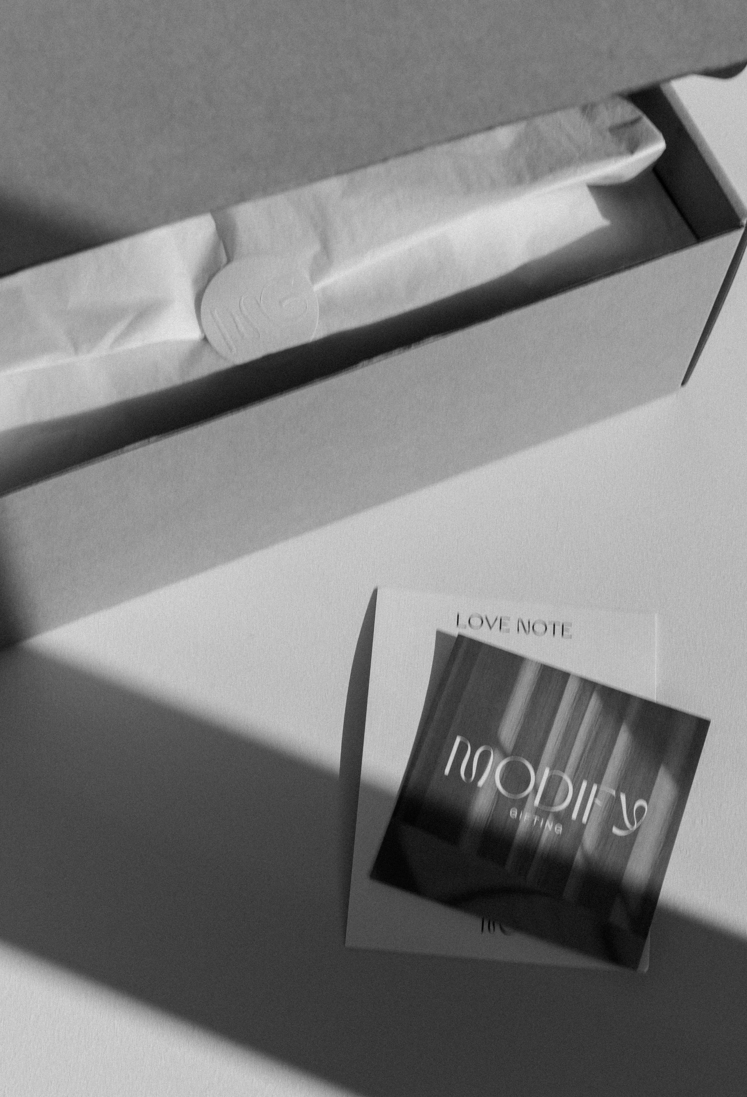 Open box with tissue paper and a Love Note card with a blurred image on white surface.