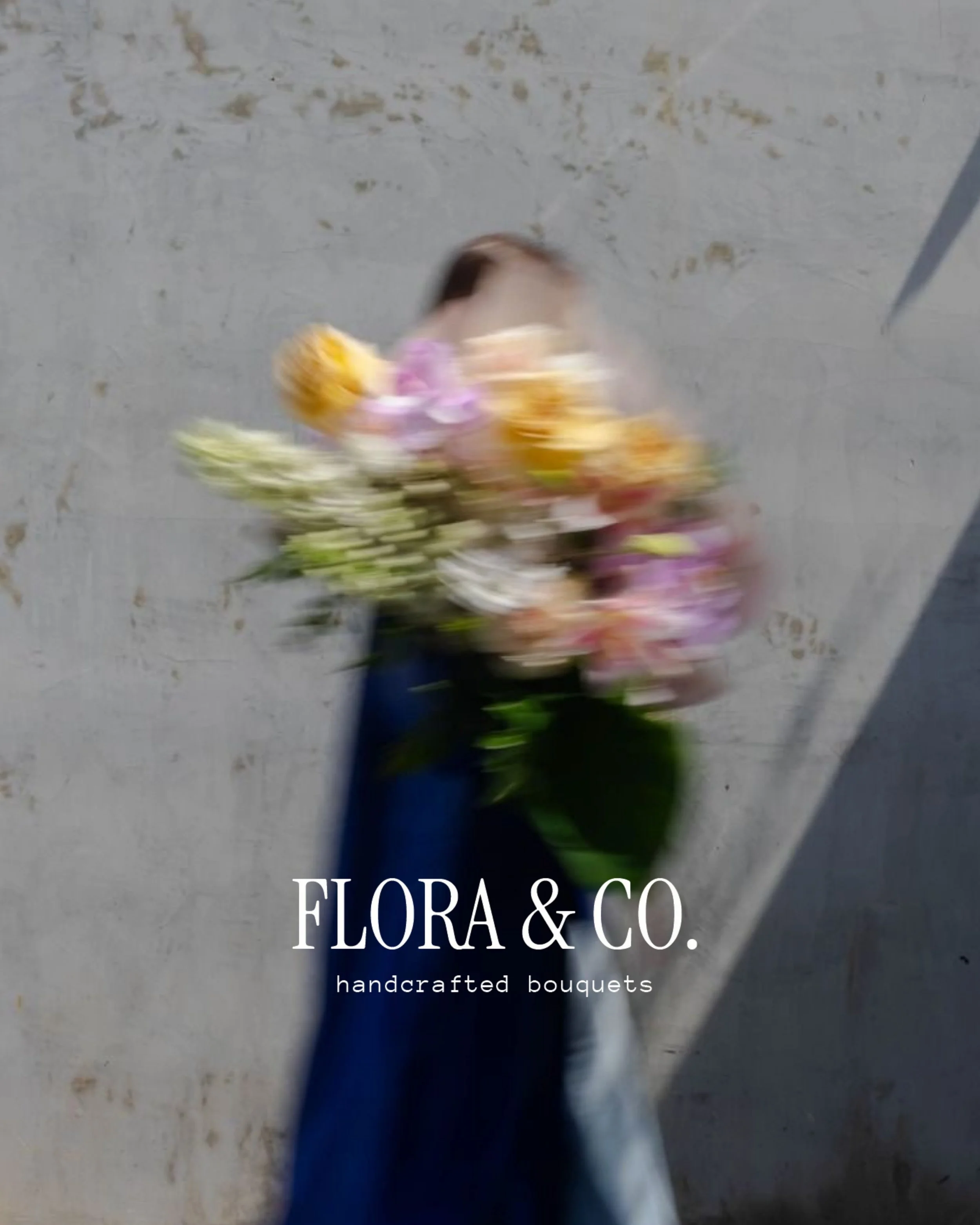 Blurred image of a person holding a bouquet of colorful flowers against a concrete wall, with text overlay that reads "FLORA & CO. handcrafted bouquets".