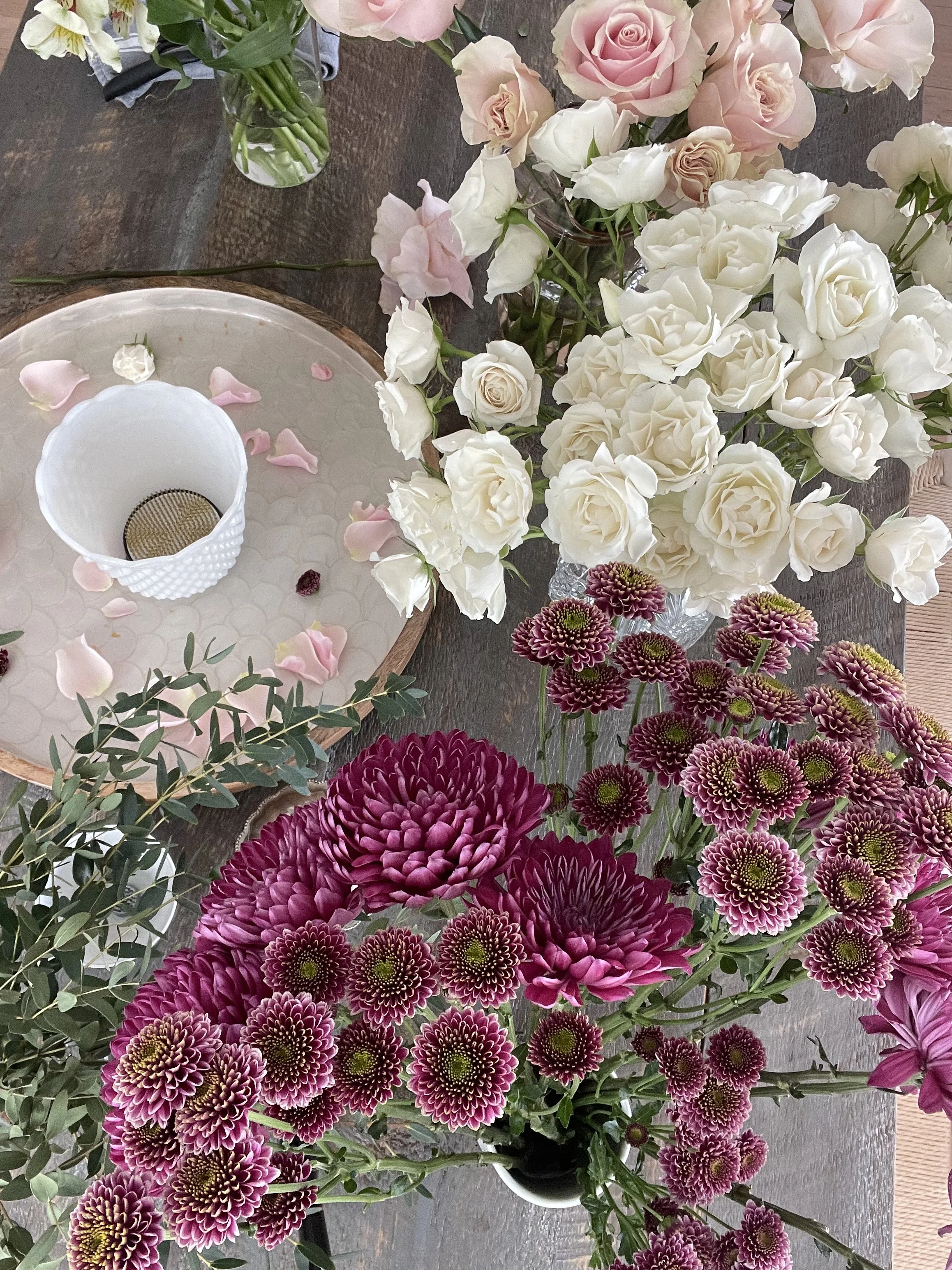A variety of floral arrangements featuring pink and white roses, pink dahlias, and purple chrysanthemums on a table.
