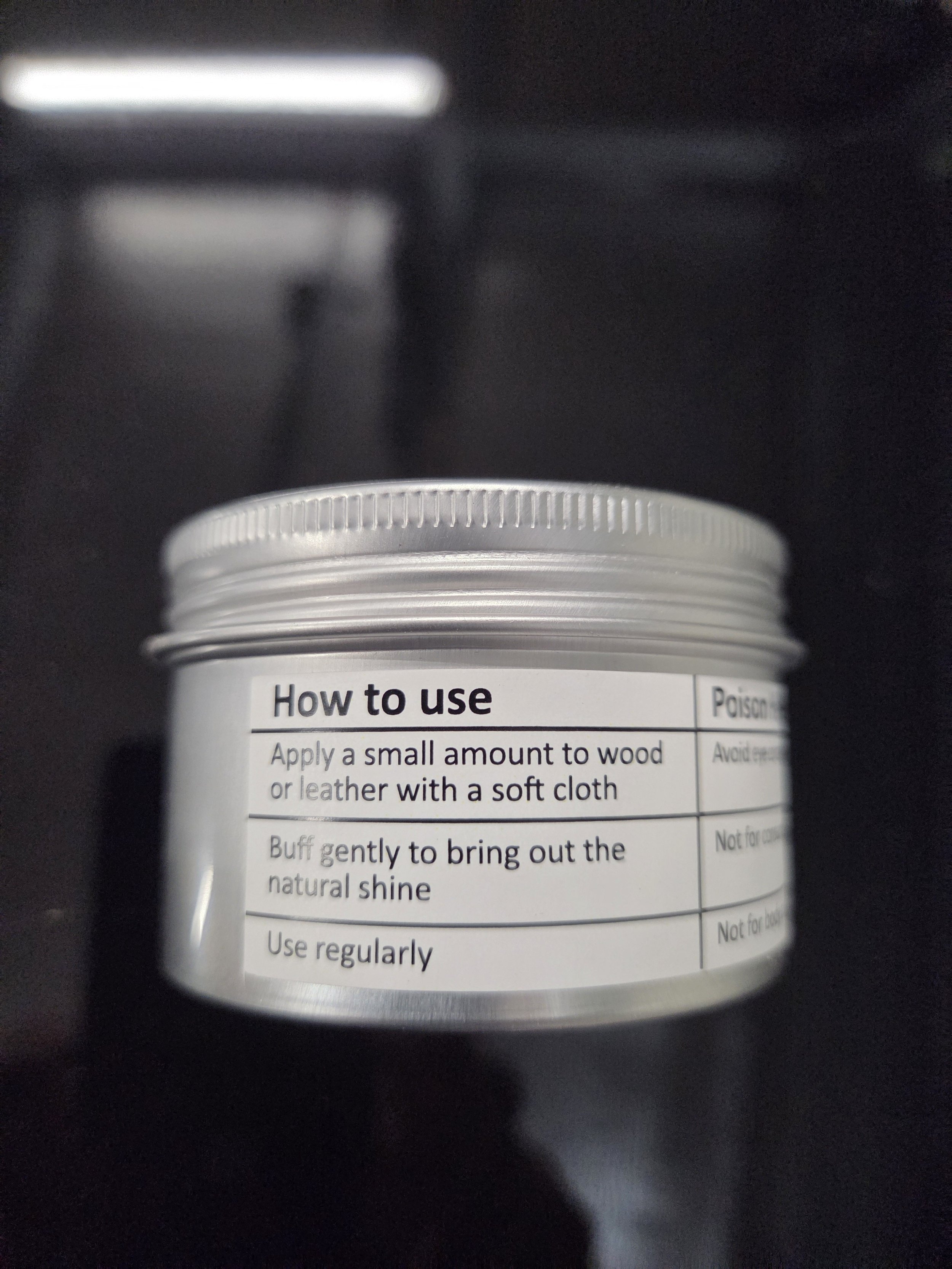 Label on a small container with instructions on how to use. Instructions include applying a small amount to wood or leather with a soft cloth, buffing gently to bring out the natural shine, and using regularly.