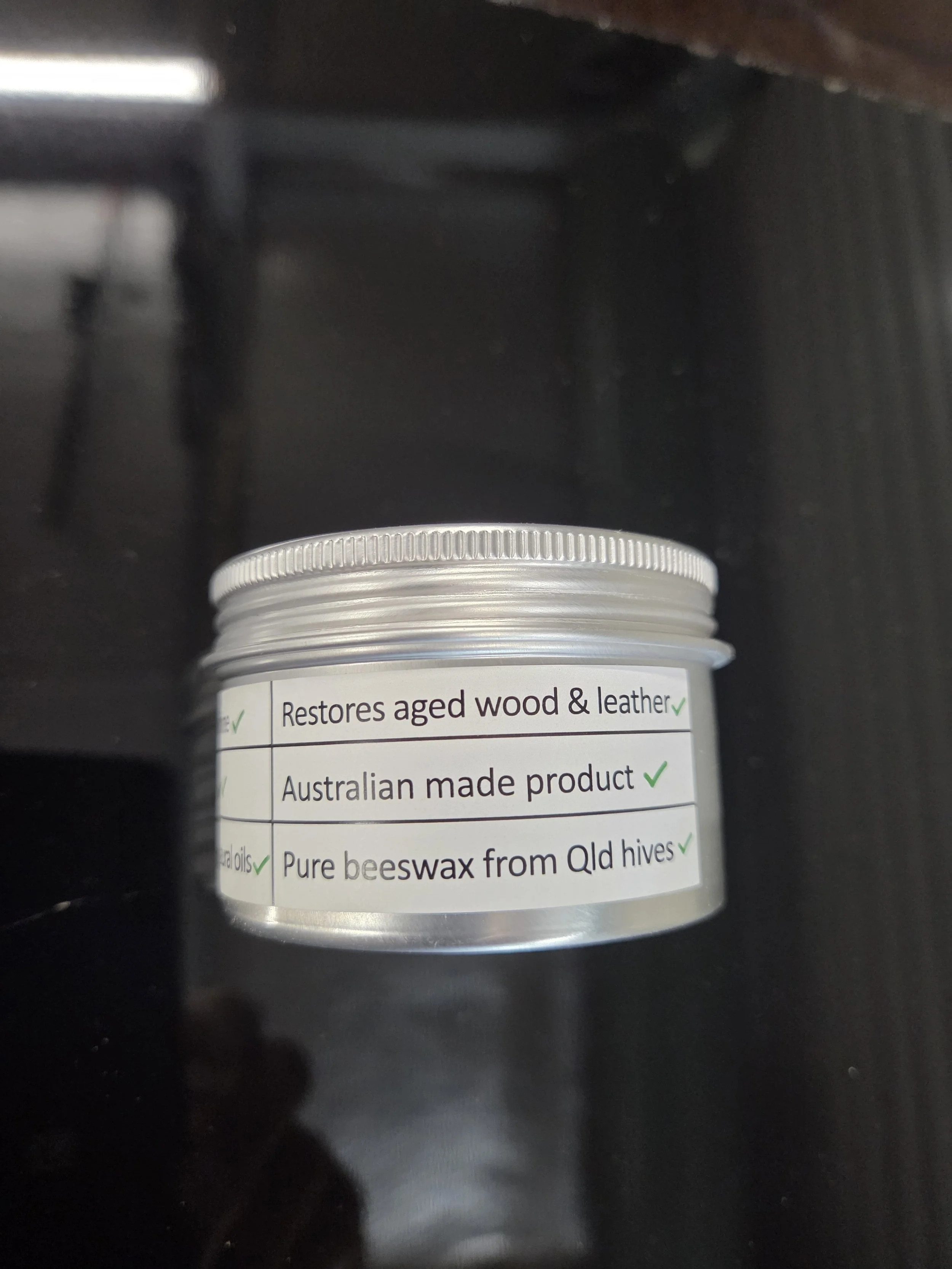 A small round container with a label mentioning it restores aged wood and leather, is an Australian made product, and contains pure beeswax from Queensland hives.