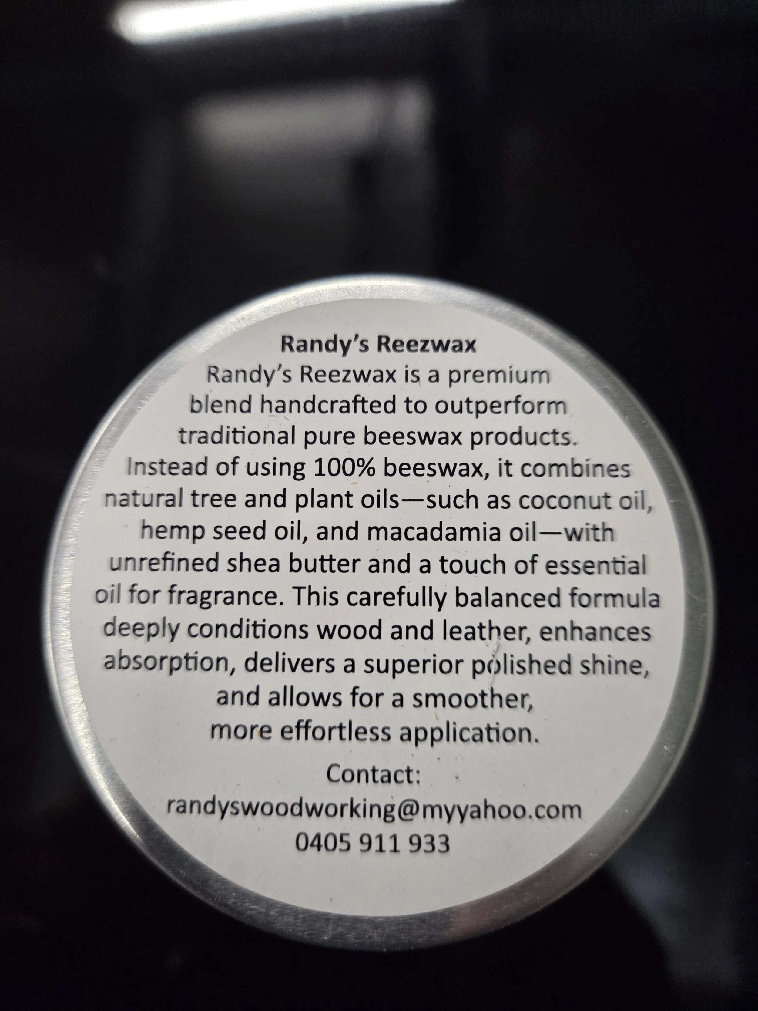 Close-up of a product label for 'Randy's Reezwax', describing it as a handcrafted beeswax blend with natural oils, shea butter, and essential oil for wood and leather conditioning, including contact information.