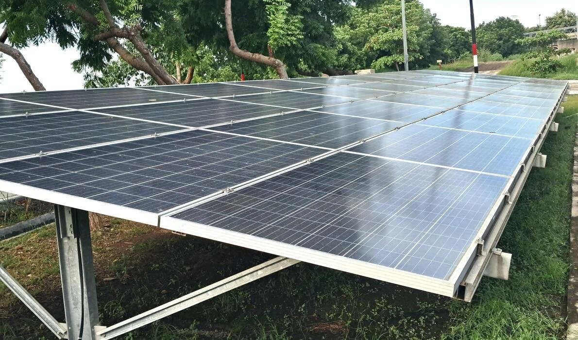 Solar panels installed outdoors on a metal frame with green trees and a pathway in the background.