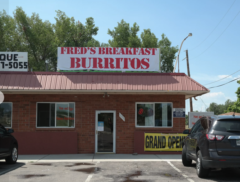 Front of a small brick building with a sign reading "Fred's Breakfast Burritos" on top and a banner announcing "Grand Opening" at the bottom.