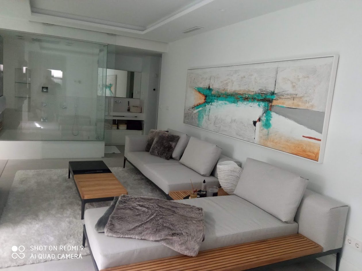 Sala moderna con sofá gris y cojines, mesa de madera y cuadros abstractos en la pared.