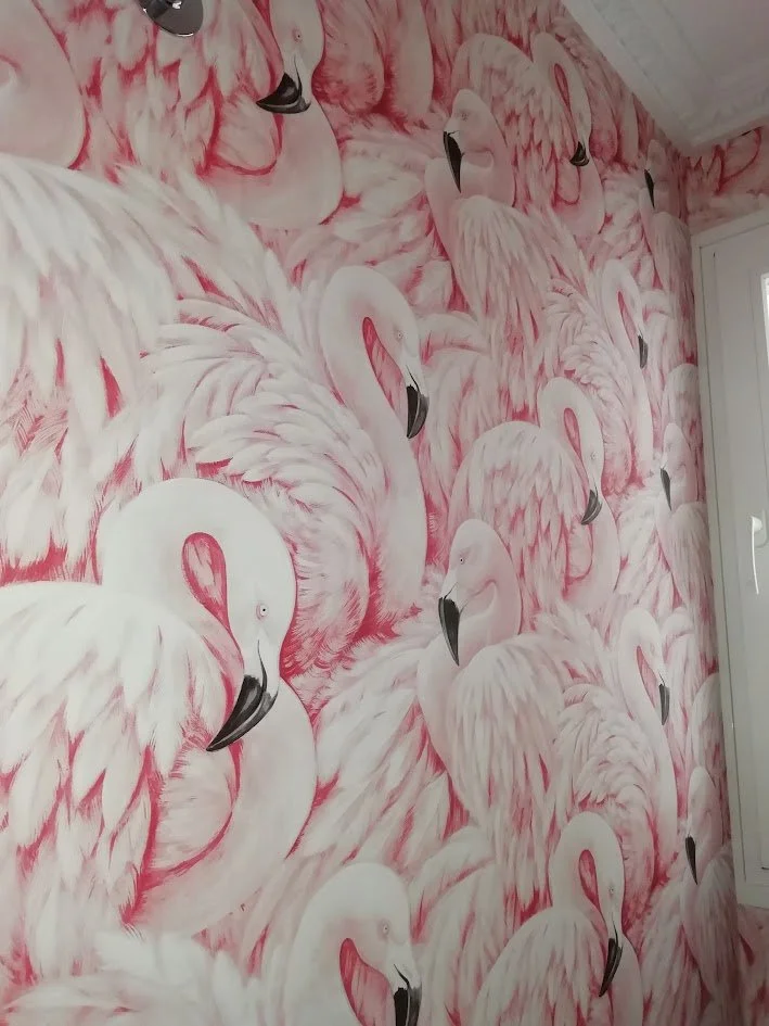 Pared decorada con mural de flamencos en tonos rosas y blancos.