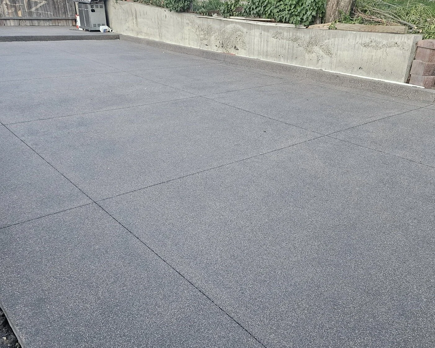 Concrete driveway with visible expansion joints, a utility box, and a concrete retaining wall with plants on top.