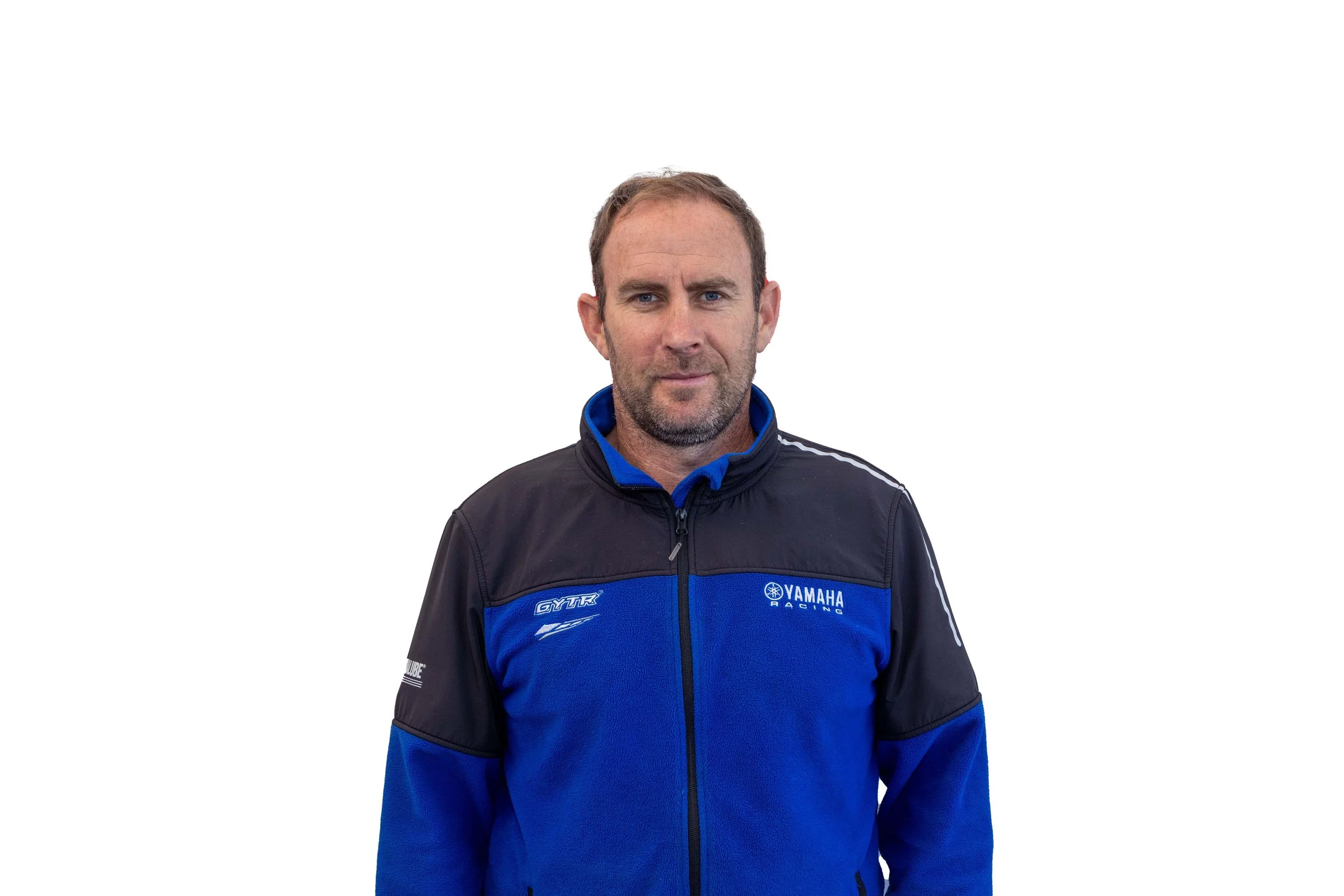 A man wearing a blue and black Yamaha racing jacket standing against a white background.