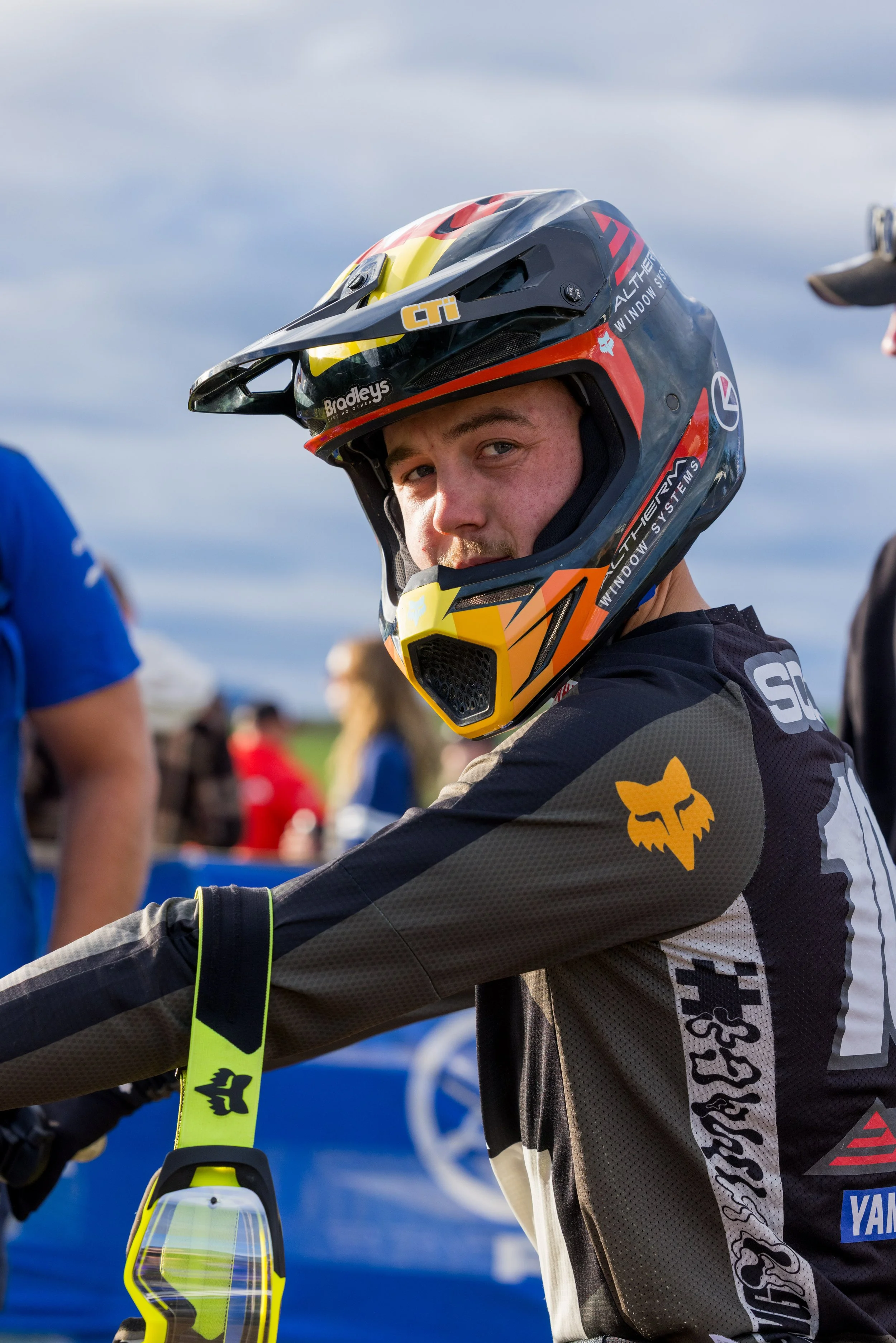 A person wearing a motocross helmet and gear, with a logo of a fox on the sleeve, at a racing event outdoors.