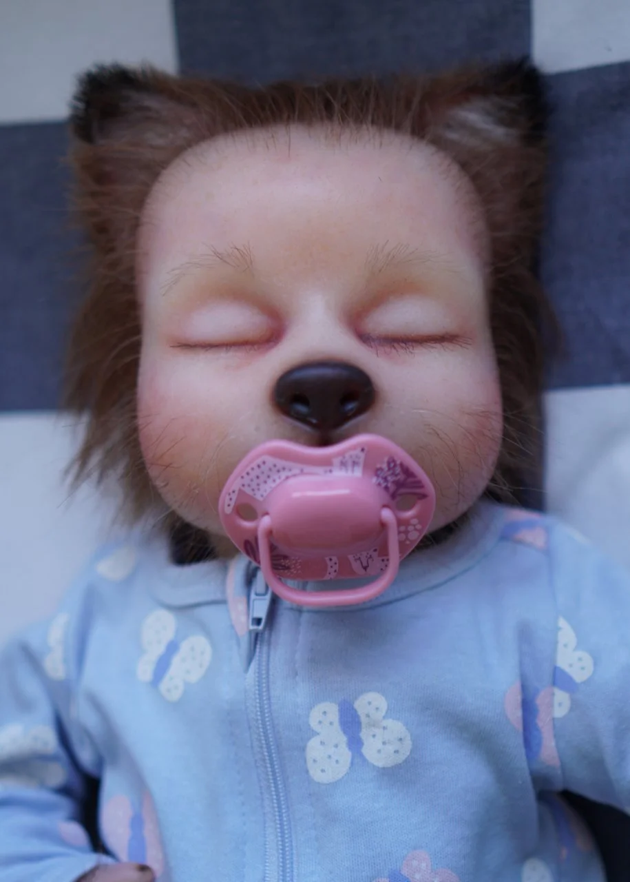 Baby fox child puppet with a pacifier, wearing a light blue onesie with butterfly prints, lying on a black and white checkered surface.