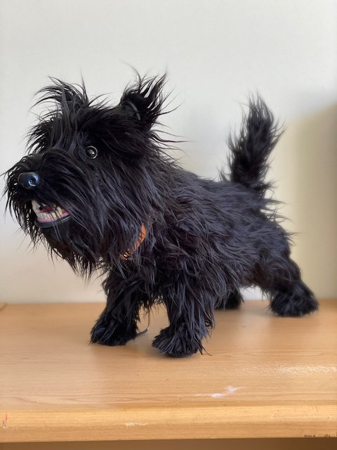 A puppet resembling a small black dog with spiky fur, standing on a wooden surface.