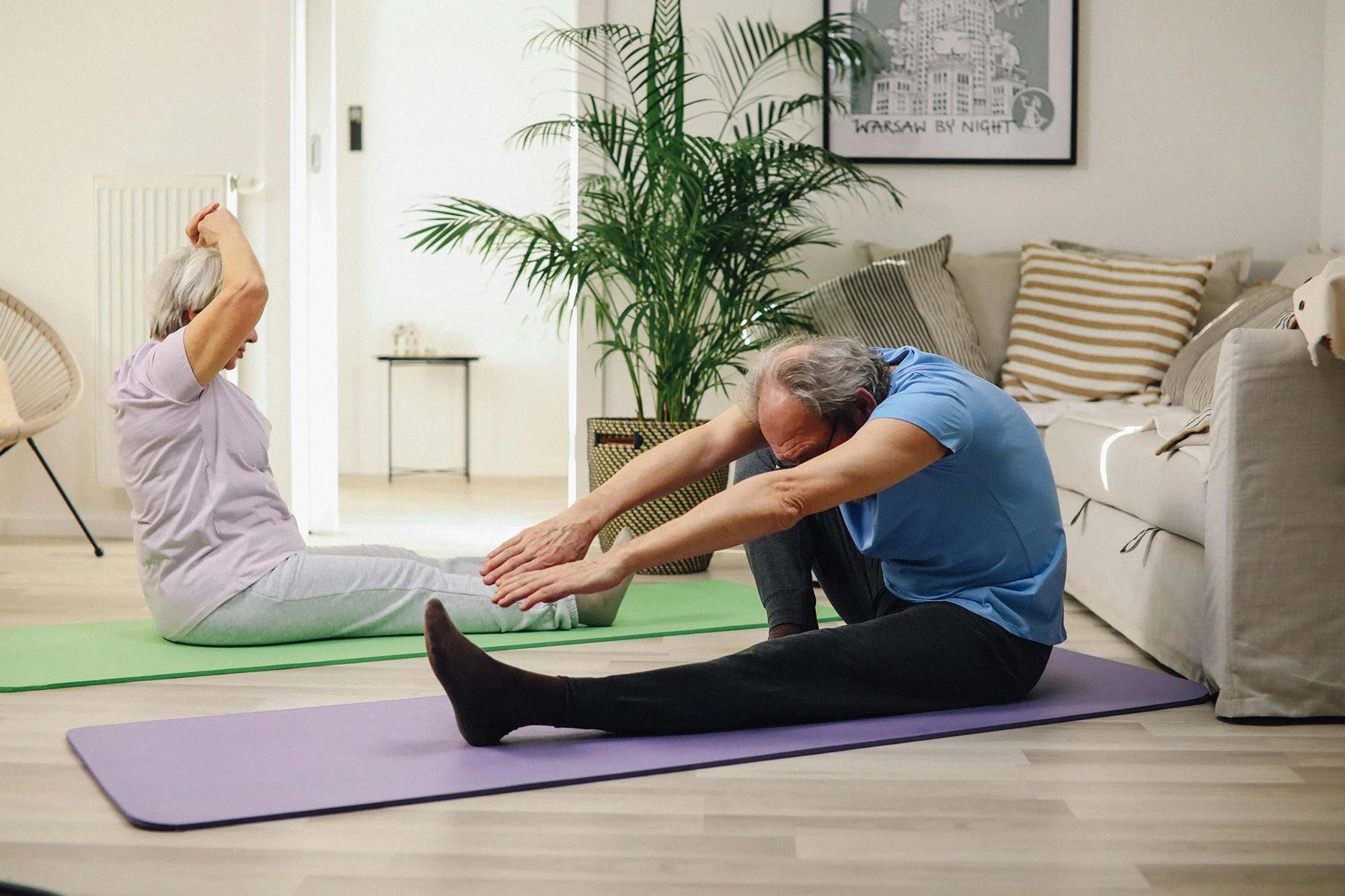 Elderly couple practicing clinical pilates moves at home on floor mats to improve mobility posture and injury prevention