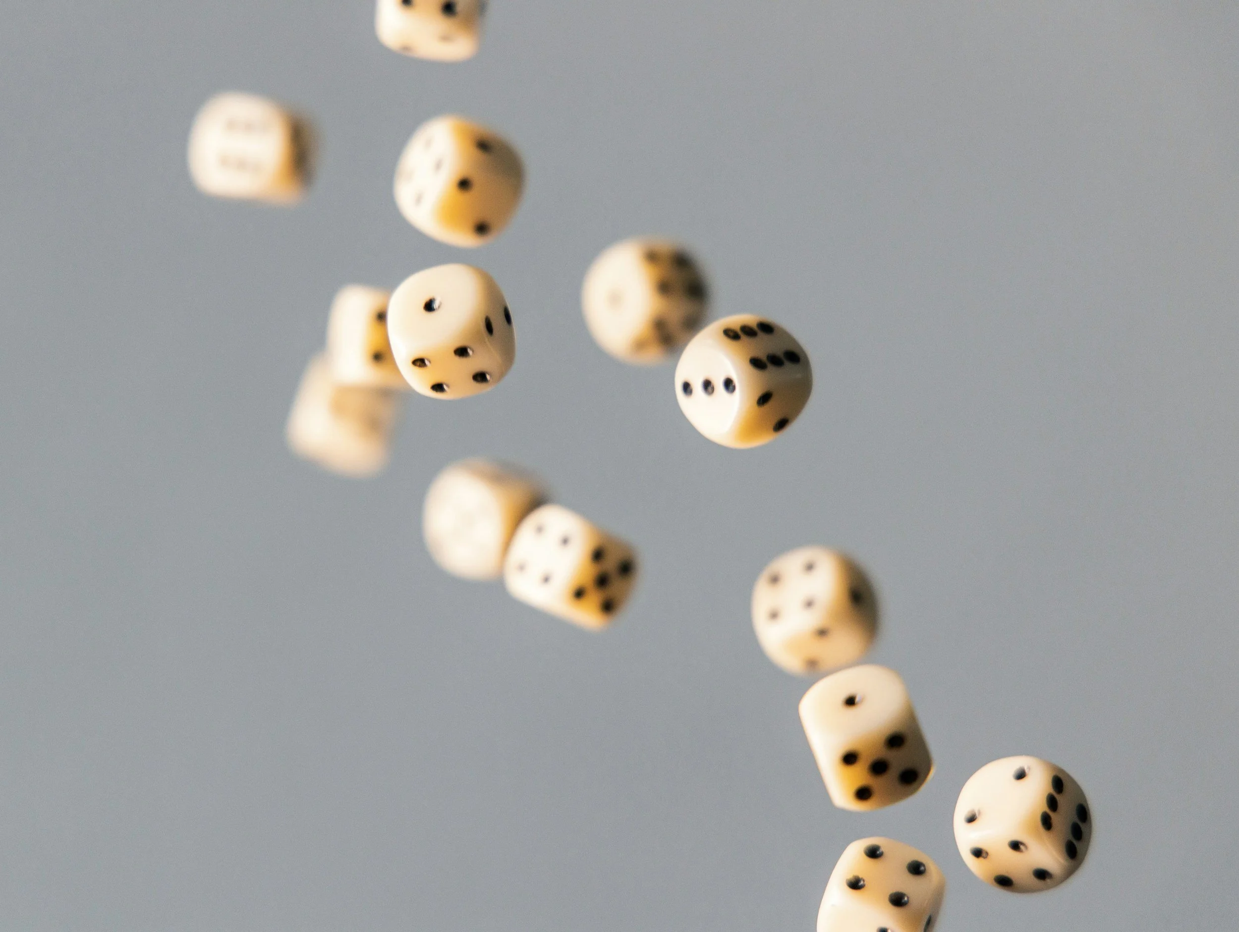 Several white dice with black pips falling against a plain gray background.