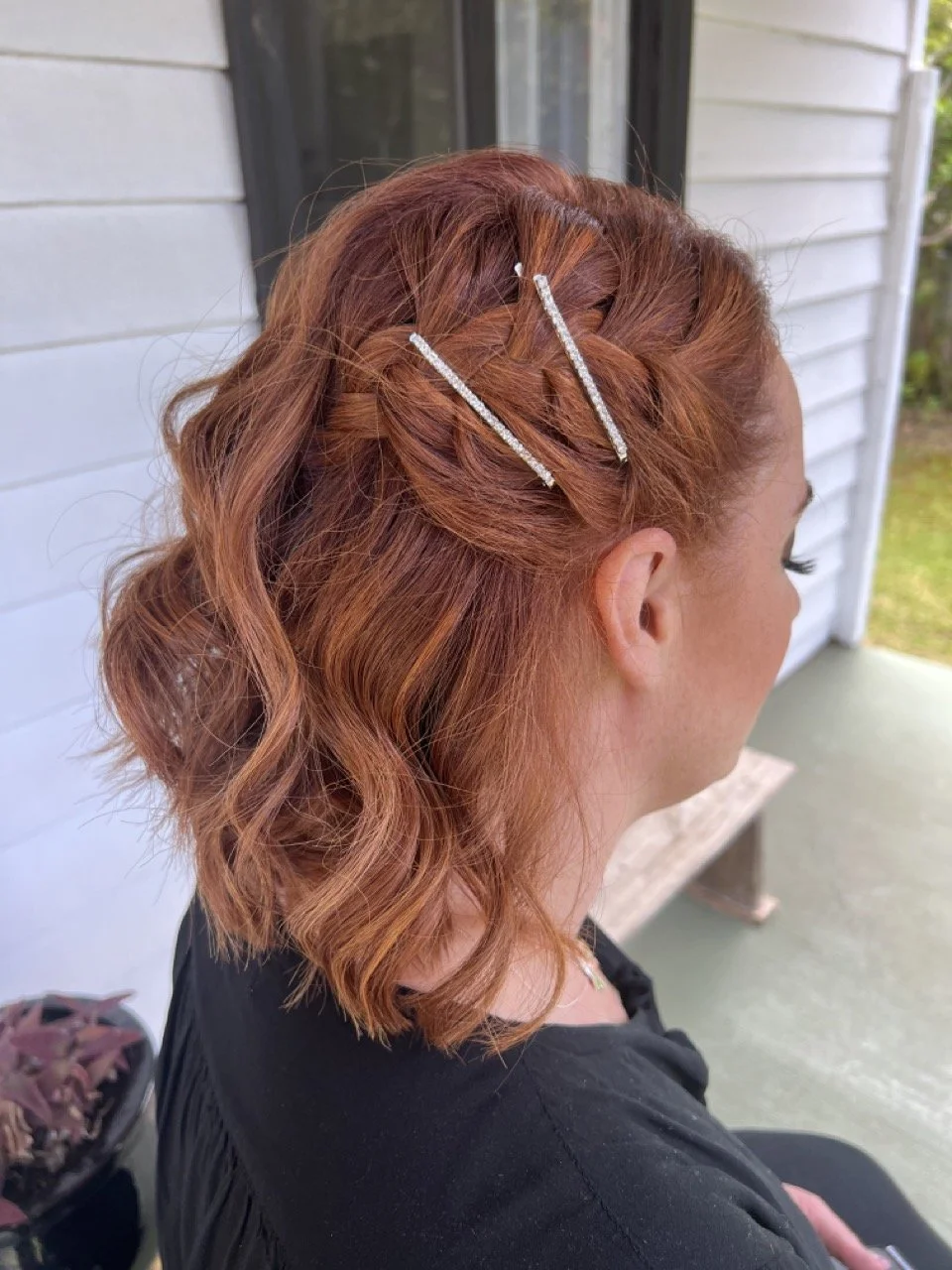 A woman with curly red hair styled in an updo with loose curls and two rhinestone hairpins.