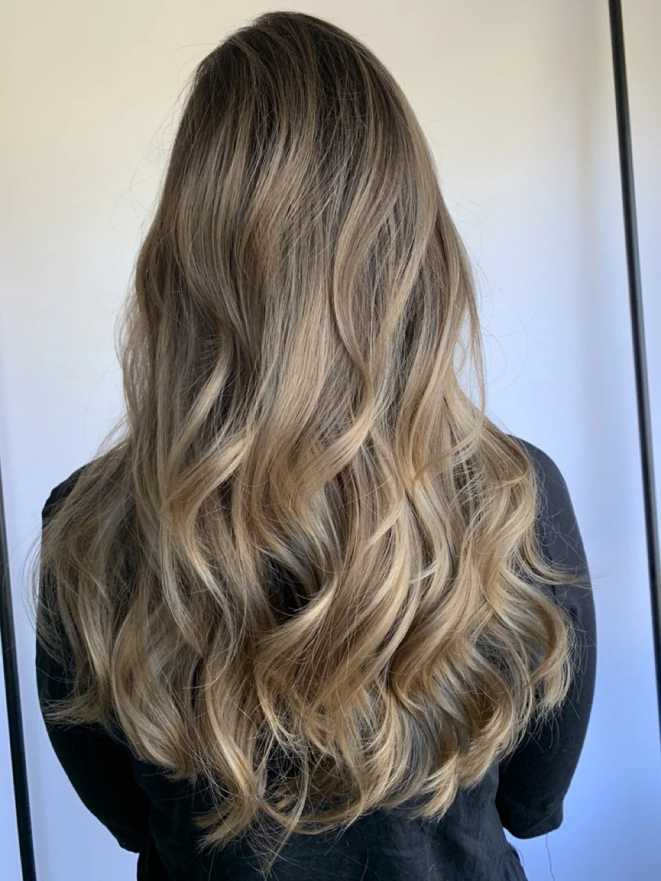 Back view of a woman with long, wavy, blonde hair wearing a black top.