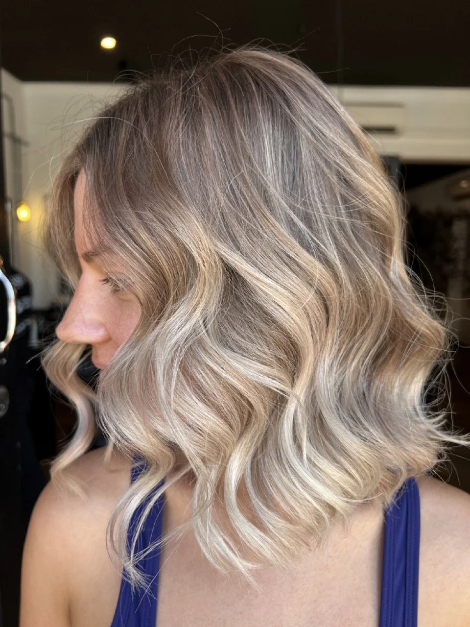Side view of a woman with blonde, shoulder-length, wavy hair in a salon.