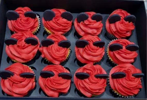 Tray of twelve cupcakes with red frosting and black oval-shaped decorations on top.