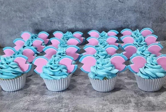 Group of cupcakes decorated with pink and blue fondant, arranged on a gray surface.