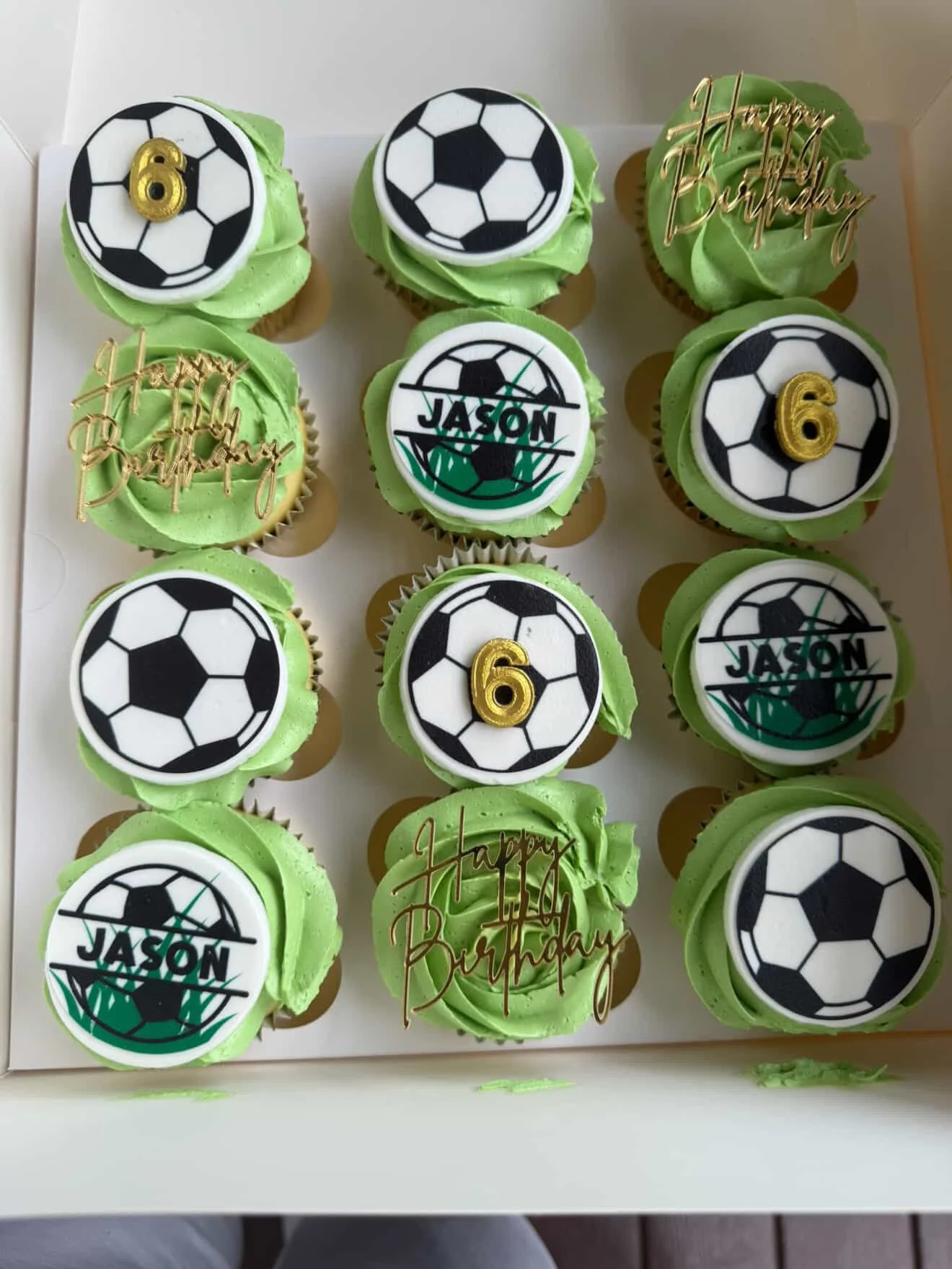 Green cupcakes decorated with soccer ball toppers, some with gold numbers 6 and 4 and gold 'Happy Birthday' toppers, arranged in a box.