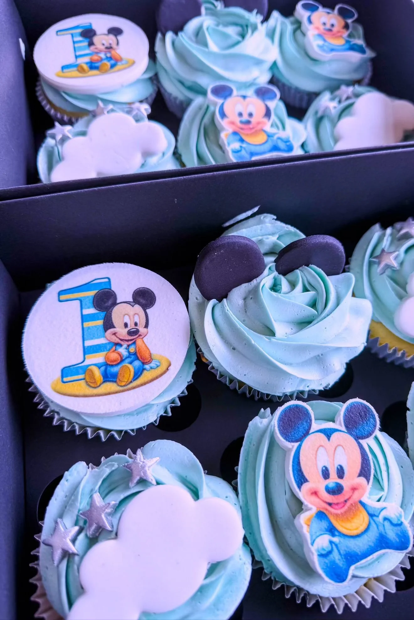 Cupcakes with blue frosting decorated with Mickey Mouse and Minnie Mouse themed edible toppers, some with star-shaped sprinkles.