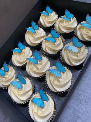 Box of twelve cupcakes topped with white frosting and blue butterfly decorations.
