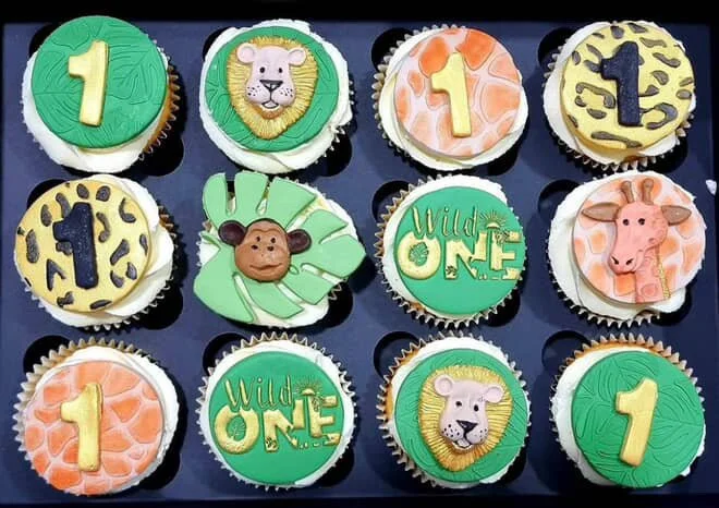 Decorative cupcakes with jungle and animal themes, featuring numbers one and three, a lion, a giraffe, a monkey, a tiger, and animal print designs.