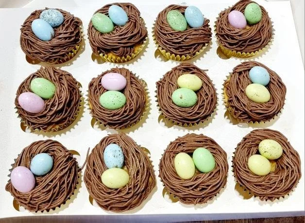 Tray of twelve chocolate nests with colorful candy eggs on top.
