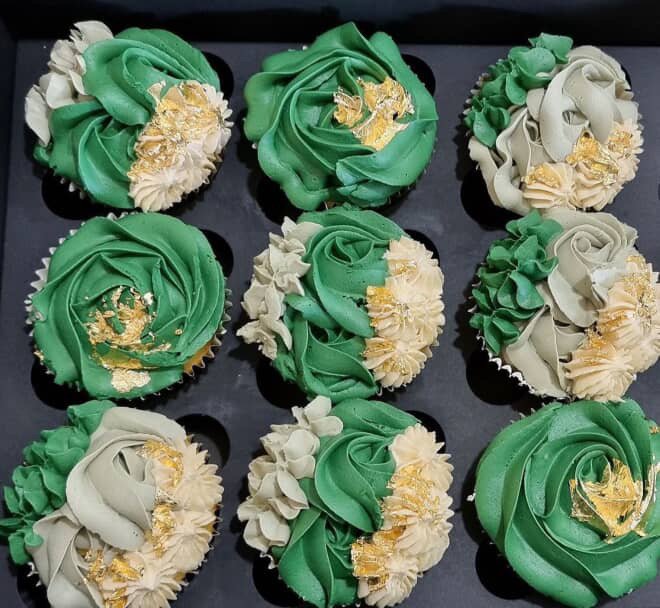 Nine cupcakes decorated with green and white frosting, gold leaf accents, arranged on a black tray.