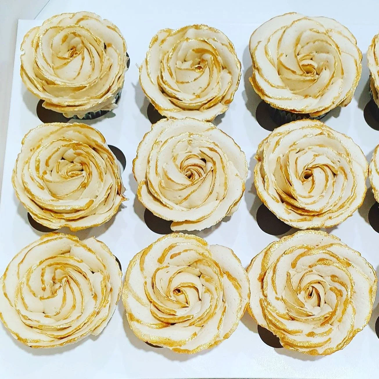 Multiple lemon-flavored cupcakes decorated with icing roses with gold accents, arranged on a white tray.