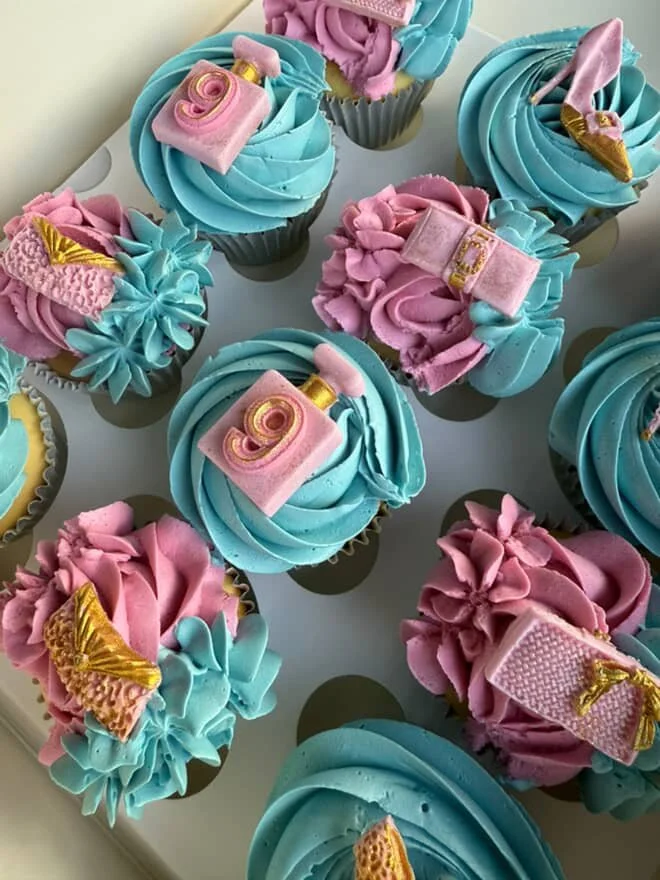 Cupcakes decorated with pink and blue frosting with miniature perfume and shoe toppers.