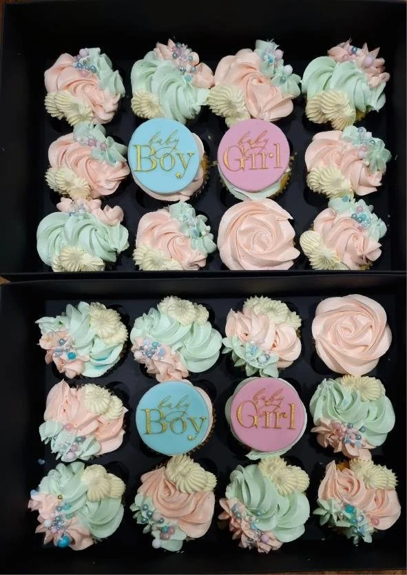 Box of pastel-colored cupcakes decorated with floral frosting and topped with 'Baby Boy' and 'Baby Girl' edible toppers.