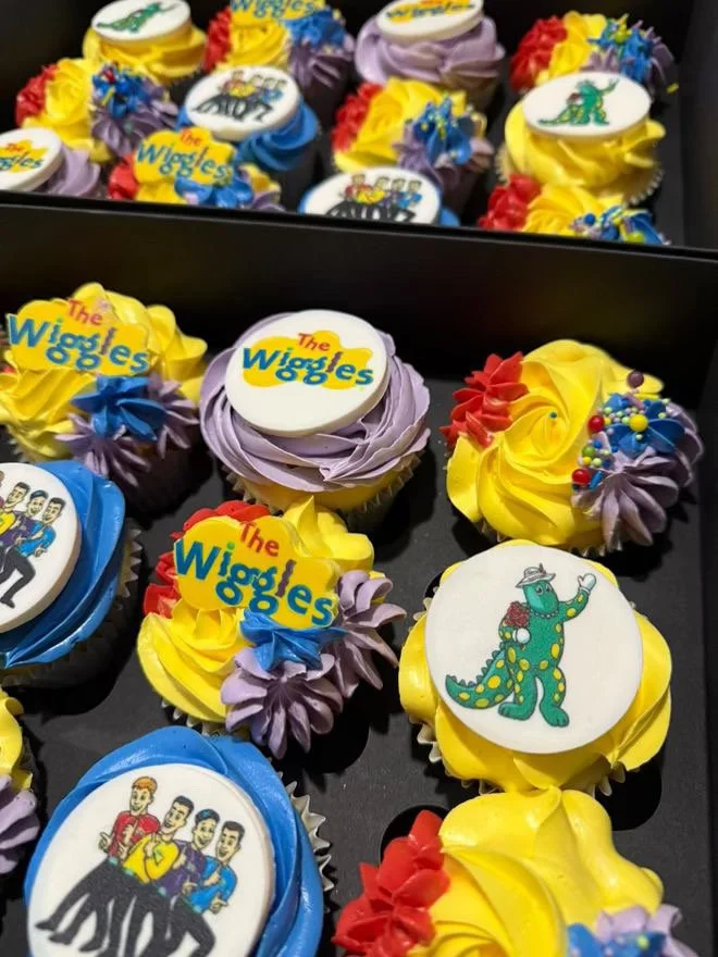 Decorated cupcakes with logos and characters from The Wiggles, featuring colorful frosting and edible toppers.
