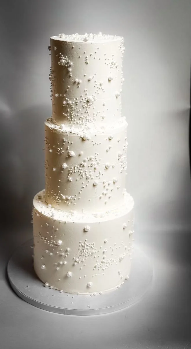 Three-tier white wedding cake decorated with small edible pearls and sugar beads.