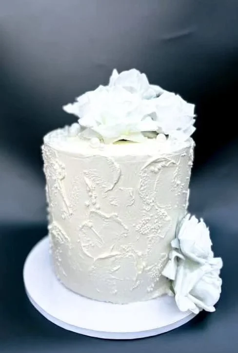 A white, textured cake with floral decorations on top and side, placed on a white cake board.