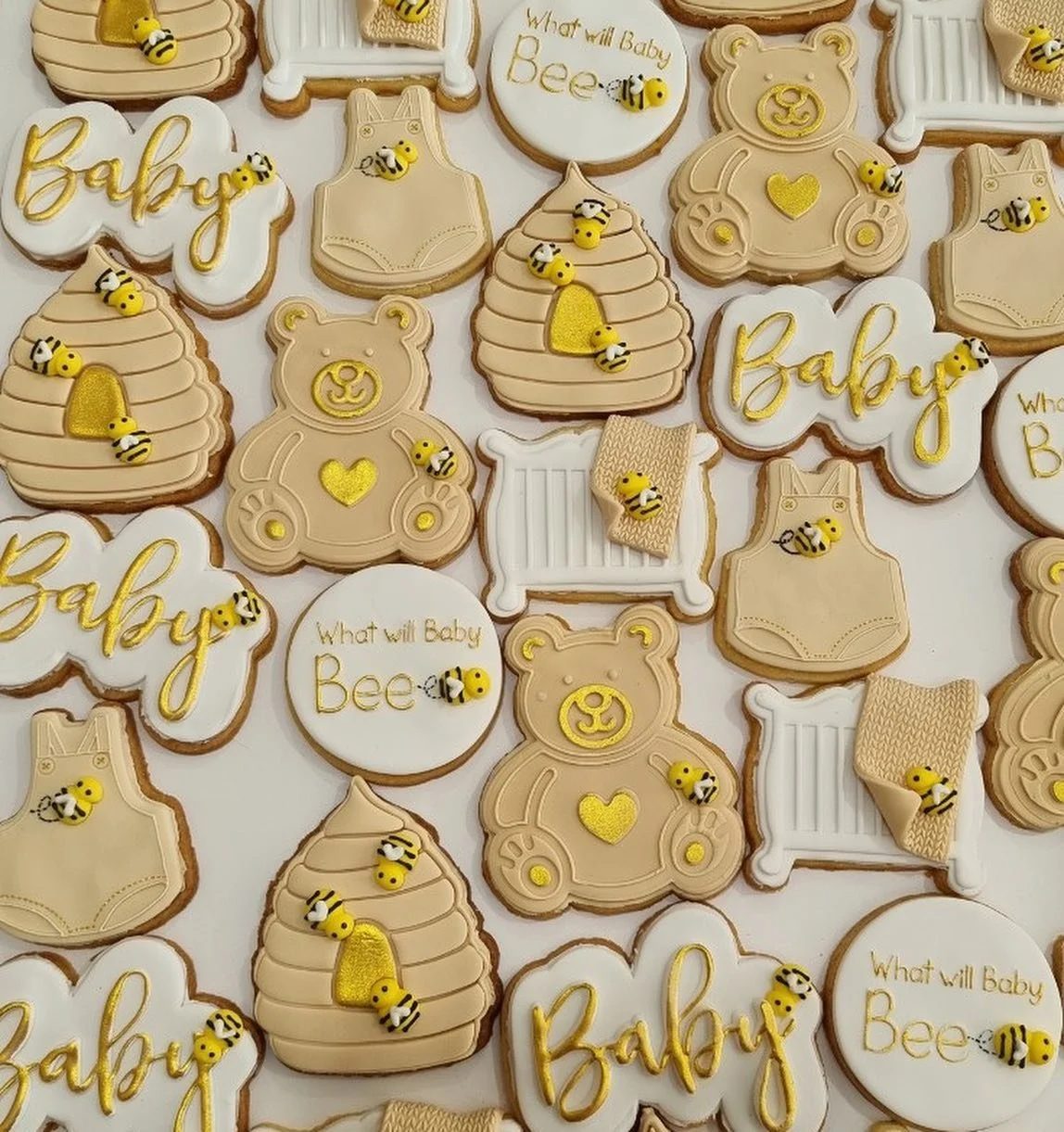 Decorative baby themed cookies in beige, white, and yellow with bee and bear motifs, some with the phrases 'Baby' and 'What will Baby Bee.'