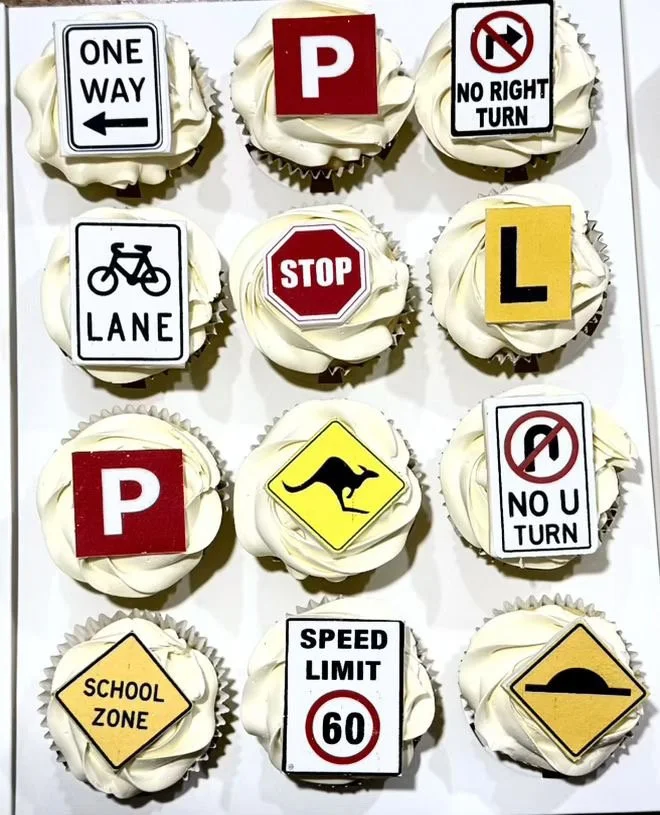 Cupcakes decorated with various road signs such as One Way, Parking, No Right Turn, Bicycle Lane, Stop, L sign, No U Turn, School Zone, Speed Limit 60, and a speed bump sign.
