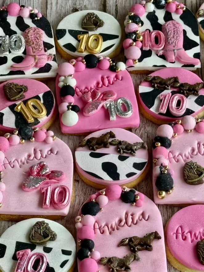 Assorted pink, black, and white decorated cookies with numbers, words, and various embellishments, celebrating a 10th birthday.