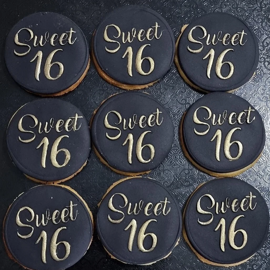A tray of nine round cookies decorated with black icing and gold lettering that says 'Sweet 16'.