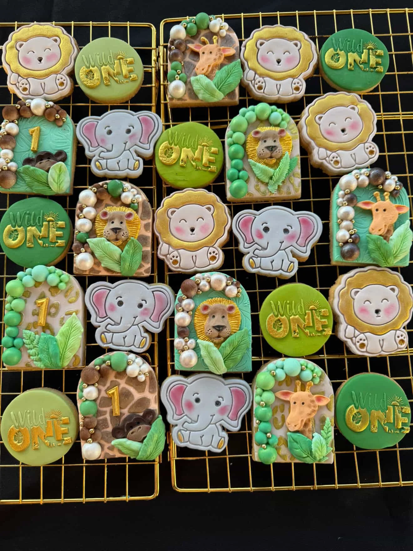 Decorated cookies with jungle and animal themes, featuring lions, elephants, giraffes, and leaves, arranged on a gold wire cooling rack.