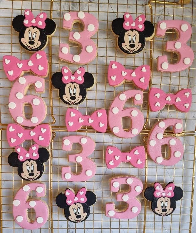 Decorative cookies featuring Minnie Mouse's face, pink numbers 3 and 6 with white polka dots, and pink bows with white polka dots, arranged on a gold wire grid.