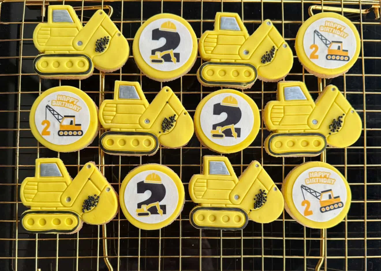 Decorative cookies with construction vehicle-themed decorations arranged on a baking rack.