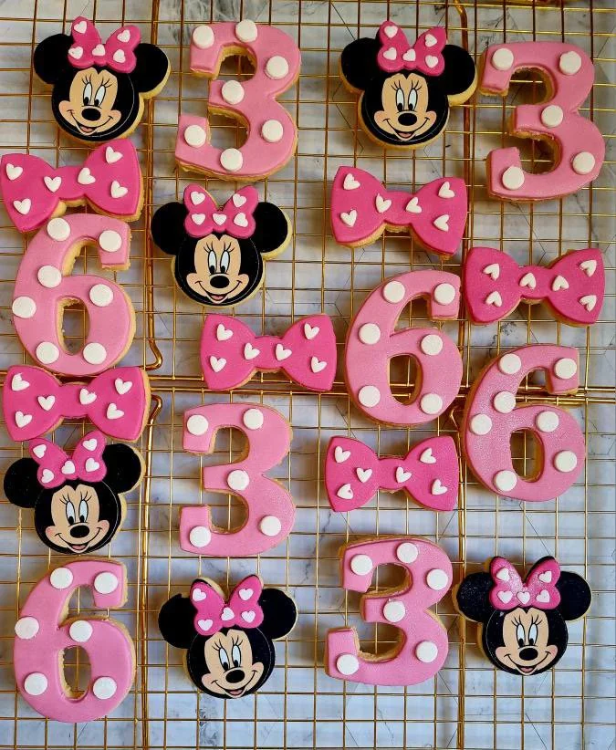 Decorated sugar cookies shaped like numbers 1 to 6, with Minnie Mouse and pink bows, displayed on a wire cooling rack.