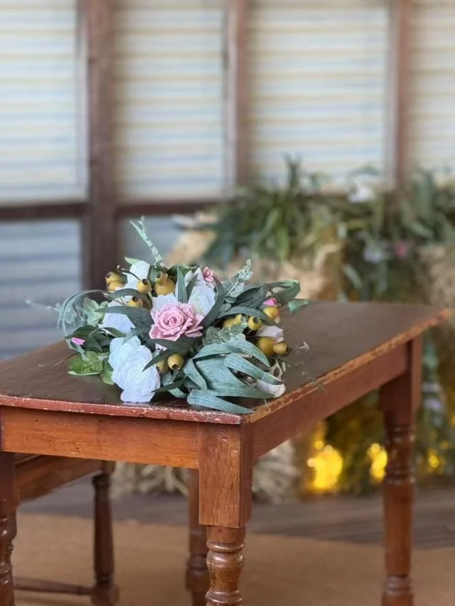 A floral arrangement with pink roses, yellow berries, and green leaves on a wooden table in a rustic setting.