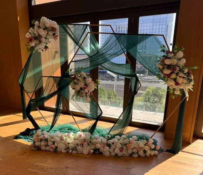 Decorative floral arrangement with pink and white flowers and teal fabric drapes near a large window.
