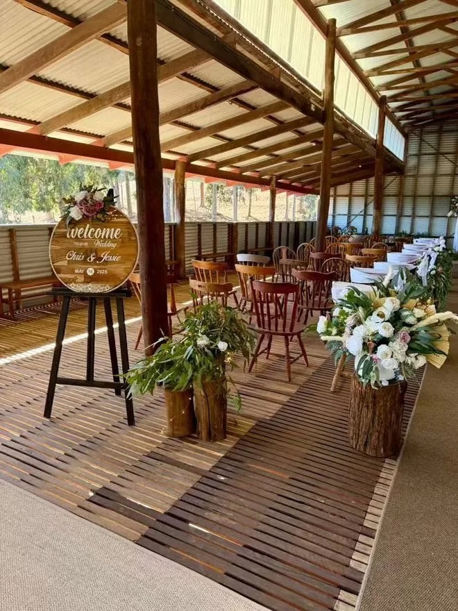 Indoor venue decorated for a wedding or event with wooden furniture and floral arrangements, including a welcome sign on a stand.