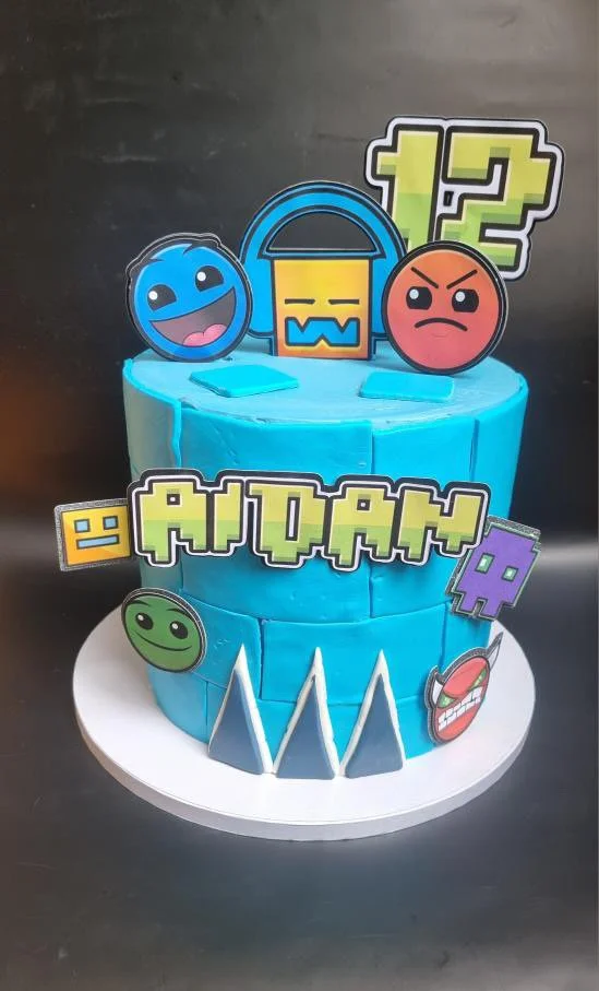 A blue Fortnite-themed birthday cake with colorful emoji and game character toppers, including a smiley face, angry face, and other pixel art decorations.