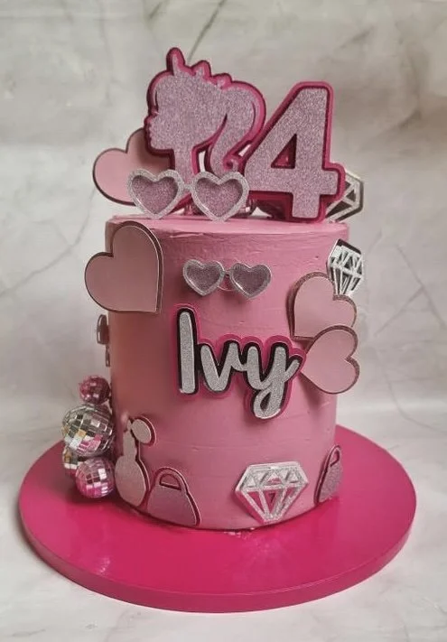 A pink birthday cake decorated with hearts, a diamond, the number 4, and the name Ivy, placed on a pink cake board.