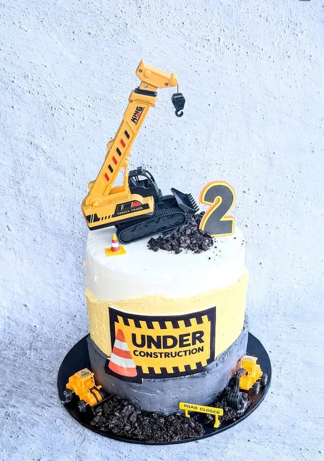 Construction-themed birthday cake with toy construction equipment, a large number 2, and construction signs, designed for a child